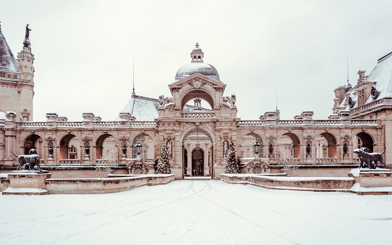 Chateau of Chantilly entrance with snow-covered courtyard and decorative statues.