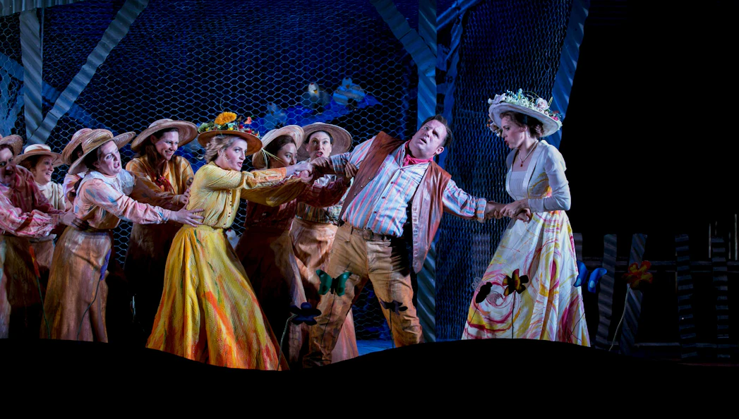 Opera performers in a scene from "The Elixir of Love" with vibrant costumes and dramatic expressions.