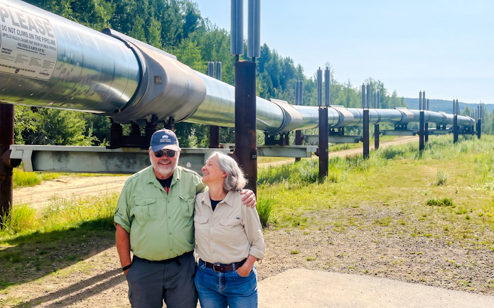 Couple standing by the Trans-Alaska Pipeline during Northern Lights & Arctic Circle Tour.