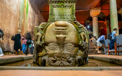 Upside down Medusa head at Basilica Cistern, Istanbul, with visitors nearby.