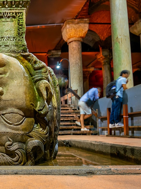 Upside down Medusa head at Basilica Cistern, Istanbul, with visitors nearby.