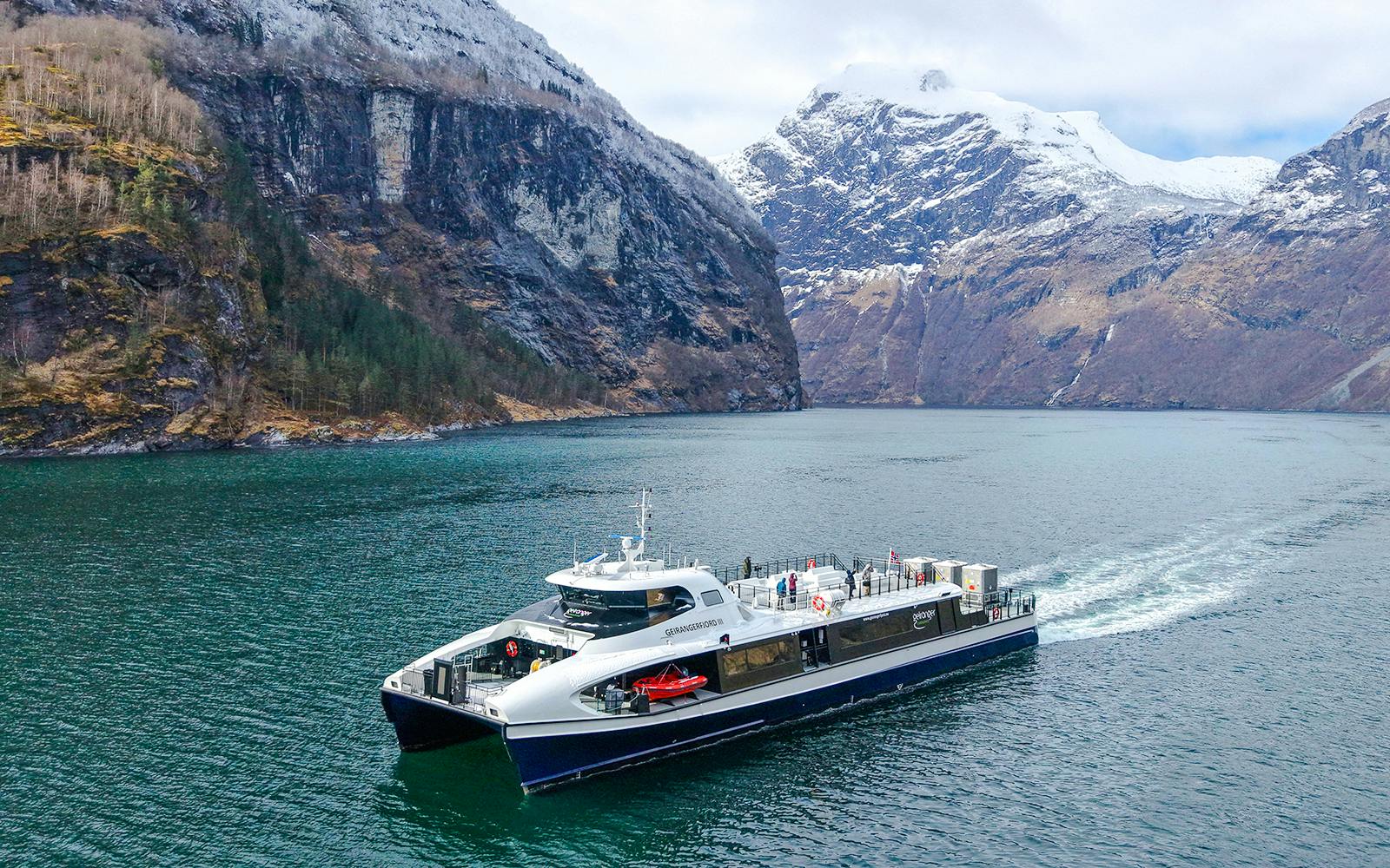 Silent Fjordcruise boat navigating through Alesund fjord, Norway, with snow-capped mountains in the background.