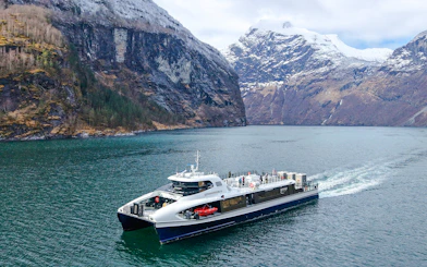 Silent Fjordcruise boat navigating through Alesund fjord, Norway, with snow-capped mountains in the background.
