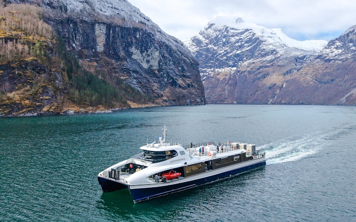 Silent Fjordcruise boat navigating through Alesund fjord, Norway, with snow-capped mountains in the background.