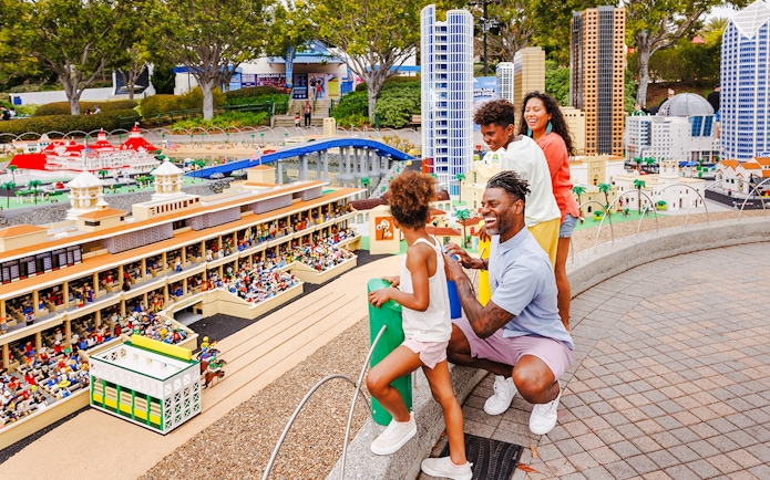 Family exploring MINILAND USA at LEGOLAND® California with LEGO cityscape in background.