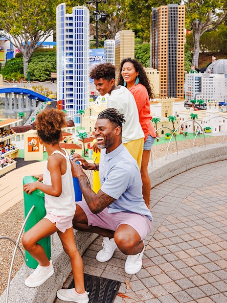 Family exploring MINILAND USA at LEGOLAND® California with LEGO cityscape in background.