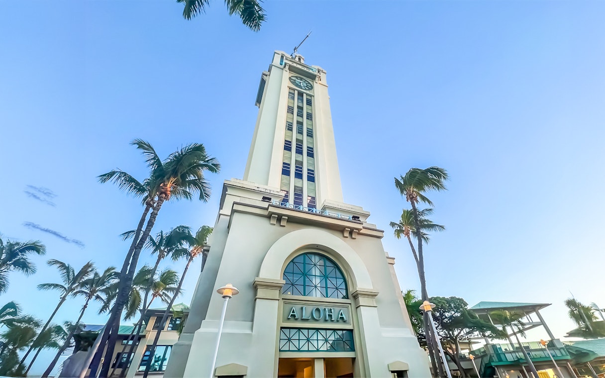Aloha Tower in Honolulu, Hawaii, surrounded by palm trees under a clear blue sky.