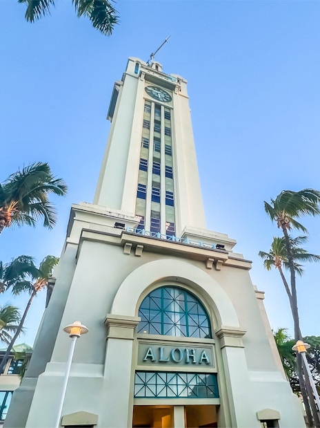 Aloha Tower in Honolulu, Hawaii, surrounded by palm trees under a clear blue sky.