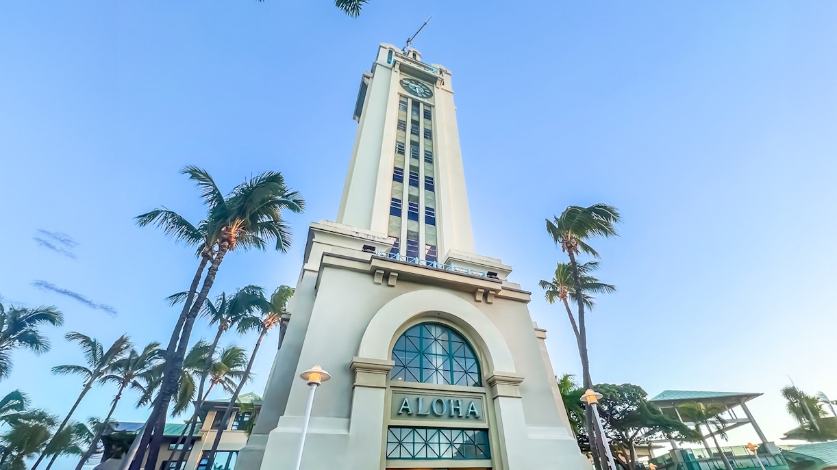 Aloha Tower in Honolulu, Hawaii, surrounded by palm trees under a clear blue sky.