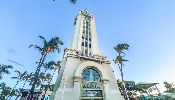 Aloha Tower in Honolulu, Hawaii, surrounded by palm trees under a clear blue sky.