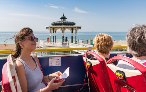 HOHO tour bus passengers at Beach Bandstand, Brighton with sea view.