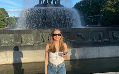 Person standing in front of Vigeland Park fountain, Oslo, holding a phone.