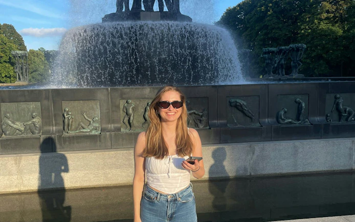 Person standing in front of Vigeland Park fountain, Oslo, holding a phone.
