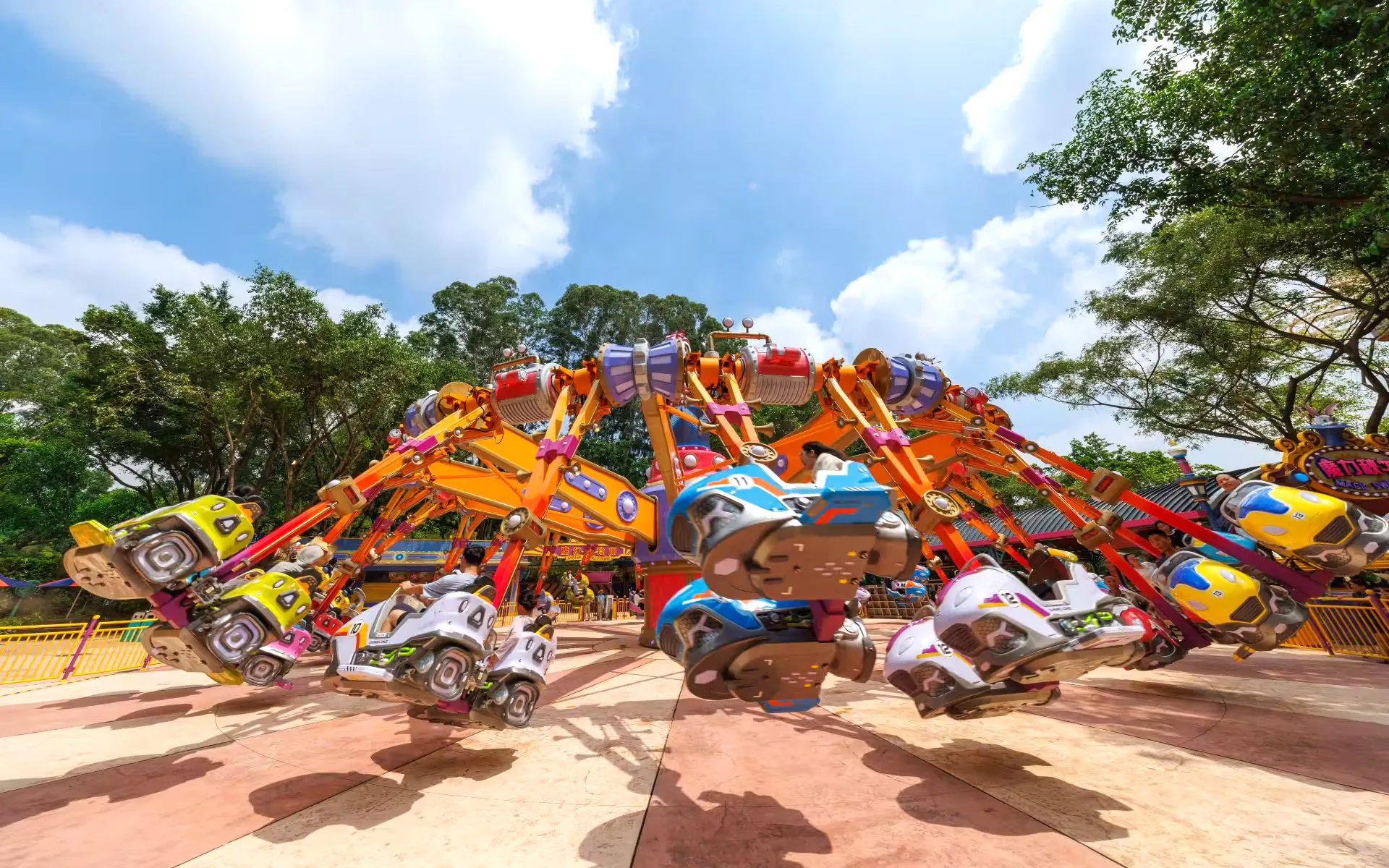 Colorful amusement ride at Chimelong Paradise with spinning cars and trees in the background.