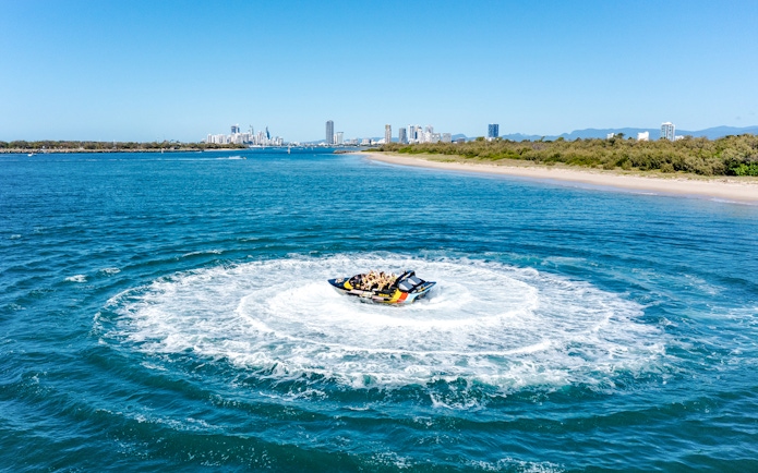 Jet boat making a circular splash on Gold Coast water with city skyline in background.