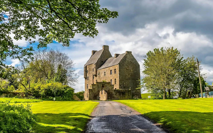 Midhope Castle in Scotland surrounded by lush greenery and a cloudy sky.
