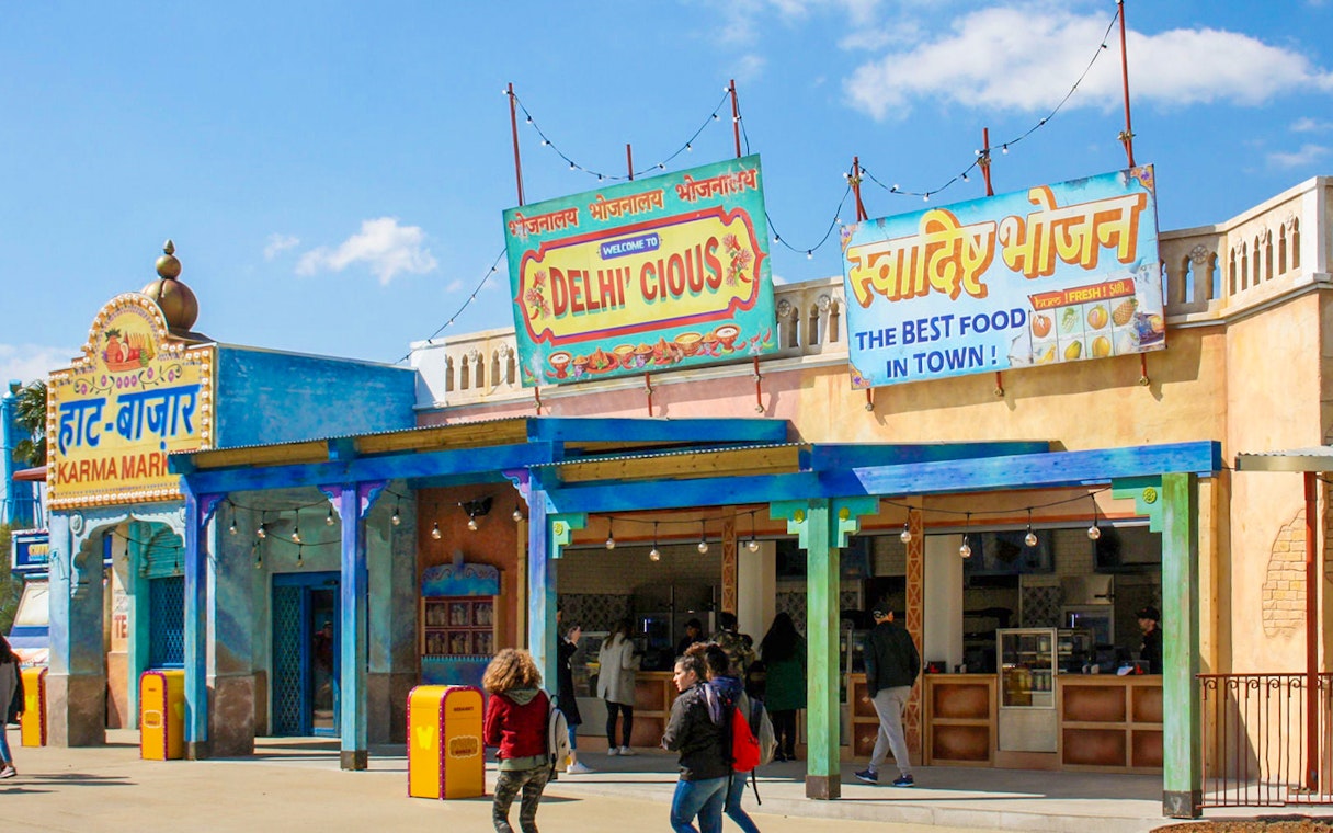 Delhicious restaurant entrance at Walibi Park with colorful signs and visitors.