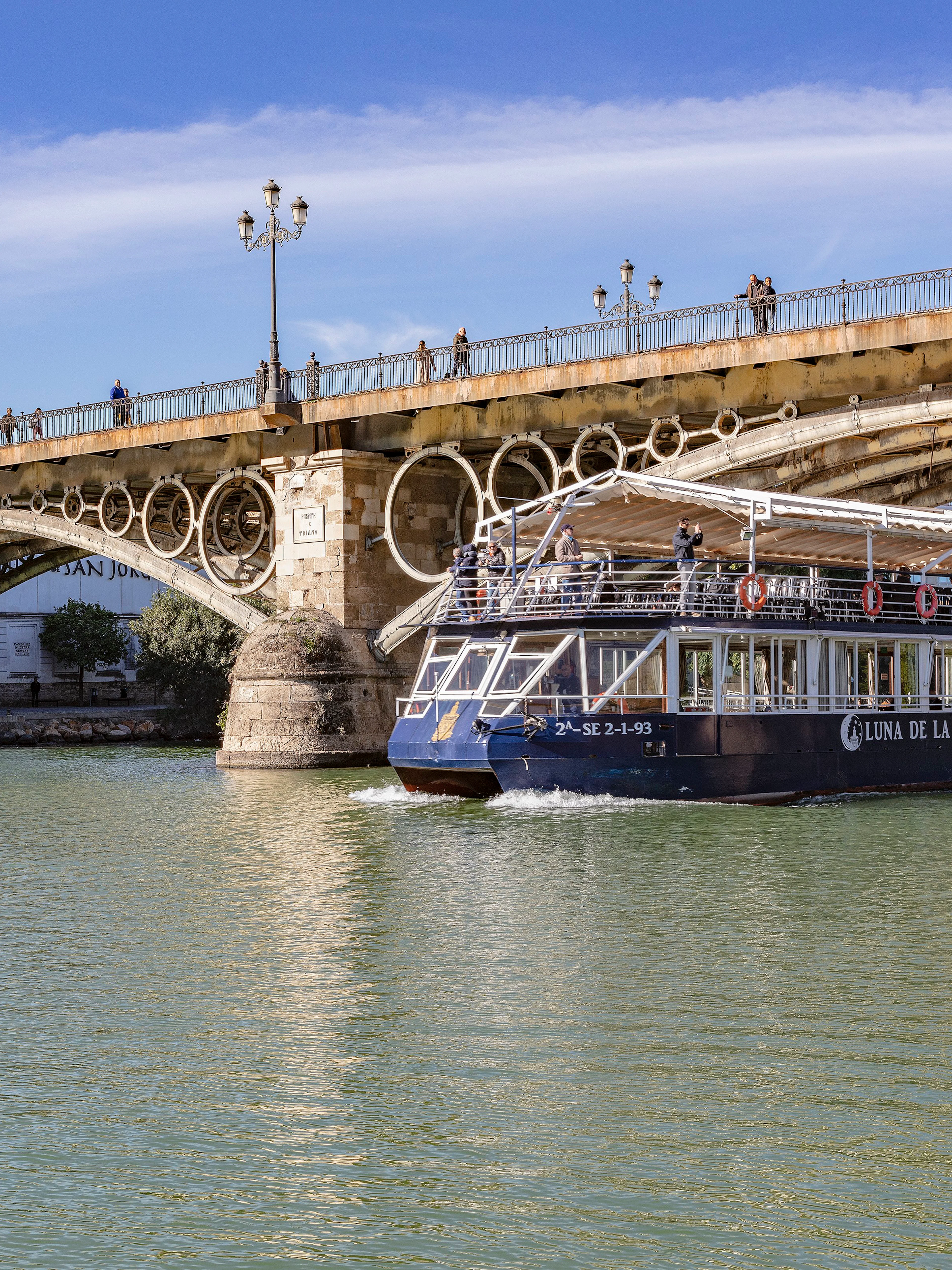 Cruise boat on Guadalquivir River passing under Triana Bridge in Seville.