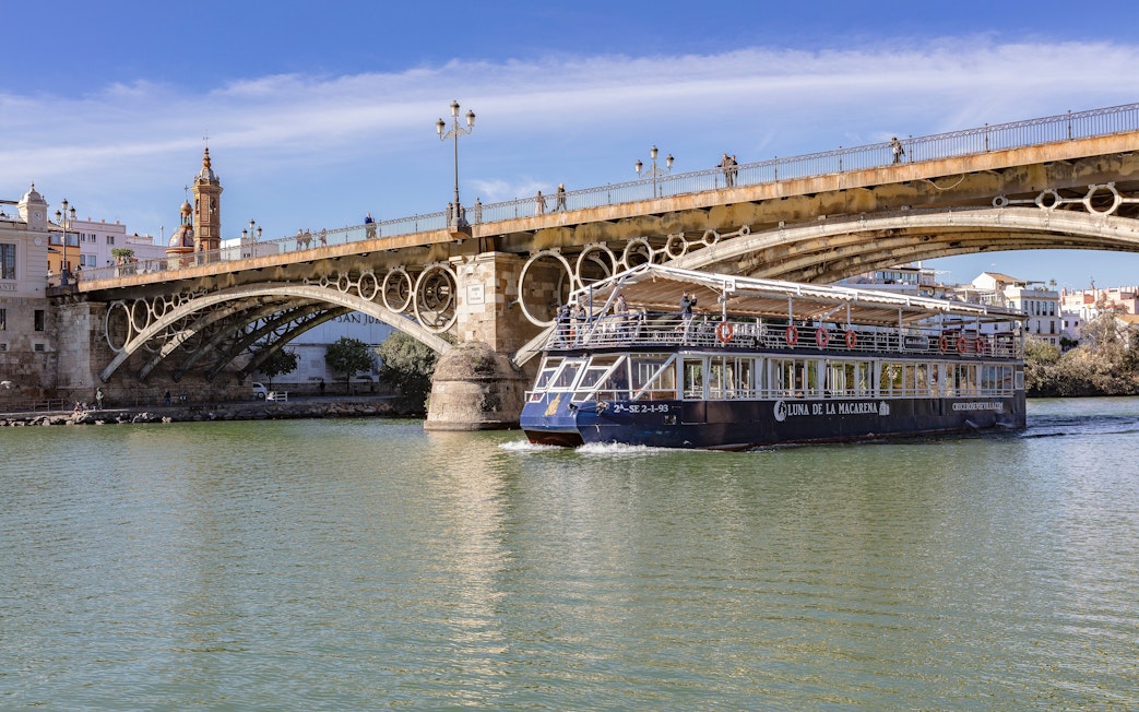 Cruise boat on Guadalquivir River passing under Triana Bridge in Seville.