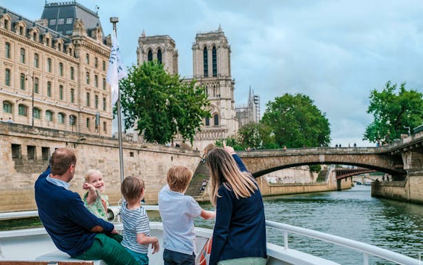 Family enjoying a guided cruise on the Seine with Notre-Dame Cathedral in view.