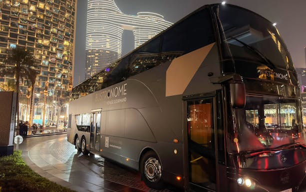 Bustronome bus offering gourmet dining experience near Burj Khalifa at night.