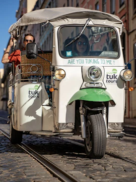 Tuk tuk on cobblestone street in Lisbon with tourists riding.