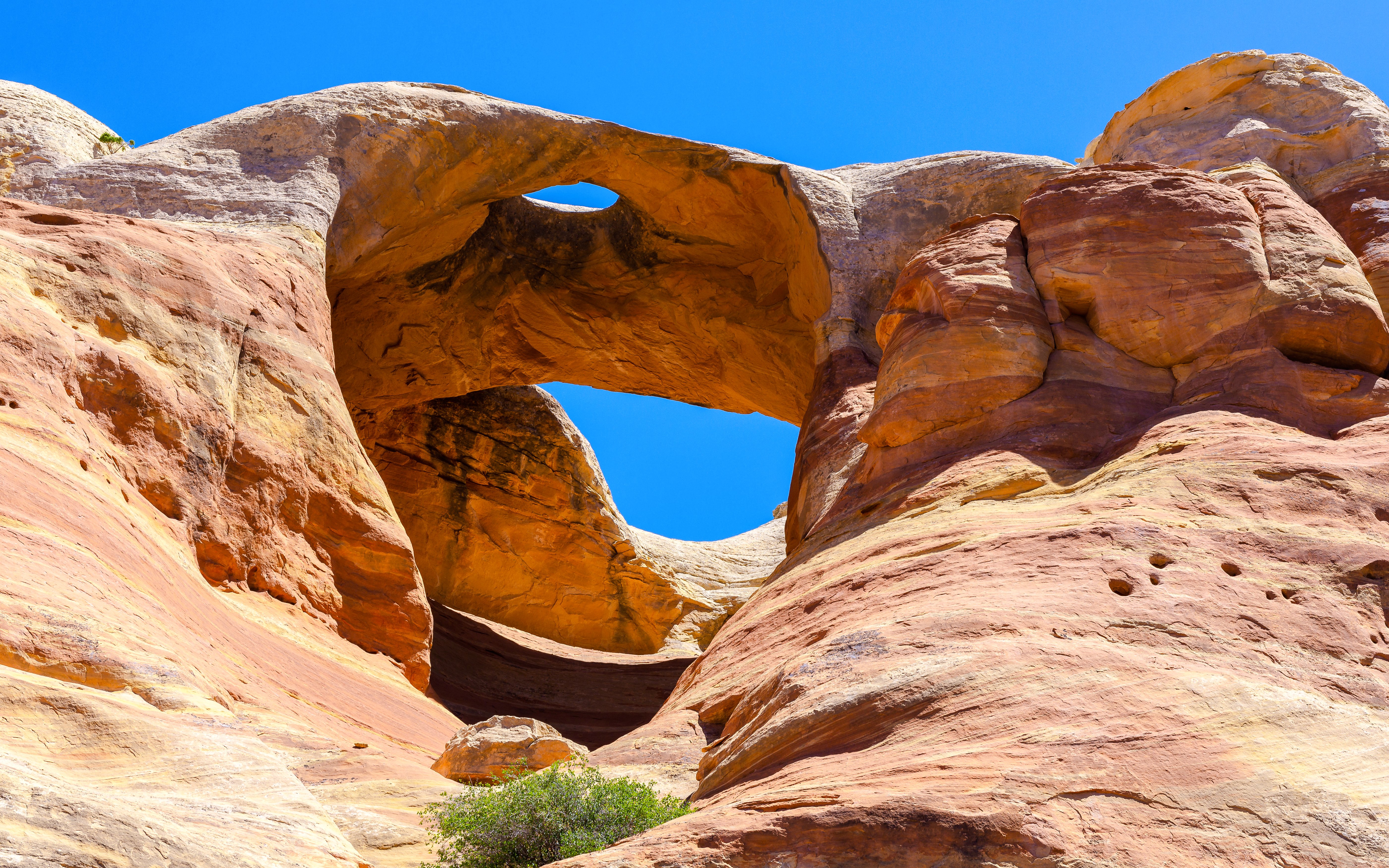 Bridge Arch rock formation in Rattlesnake Canyon under clear blue sky.