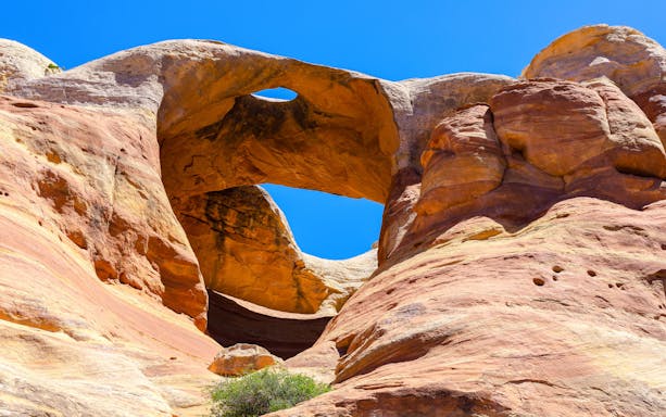 Bridge Arch rock formation in Rattlesnake Canyon under clear blue sky.