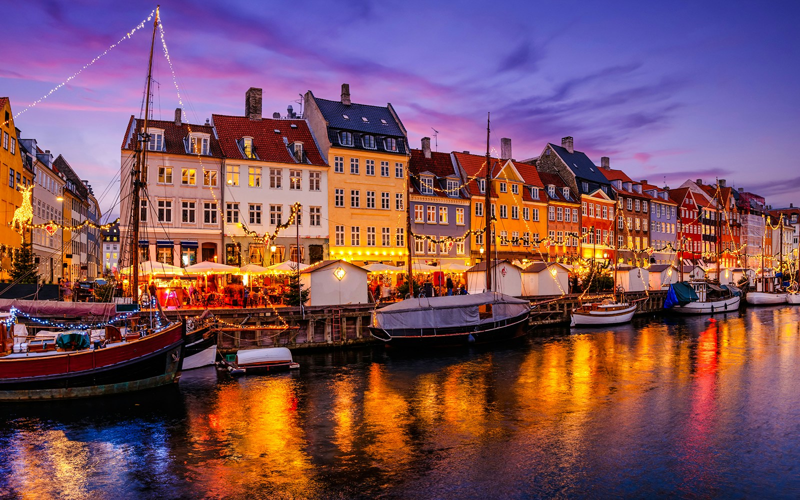 Nyhavn canal in Copenhagen with Christmas lights reflecting on the water during a winter evening.