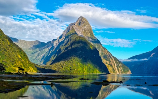 Mitre Peak reflecting in Milford Sound, New Zealand, under a clear blue sky.