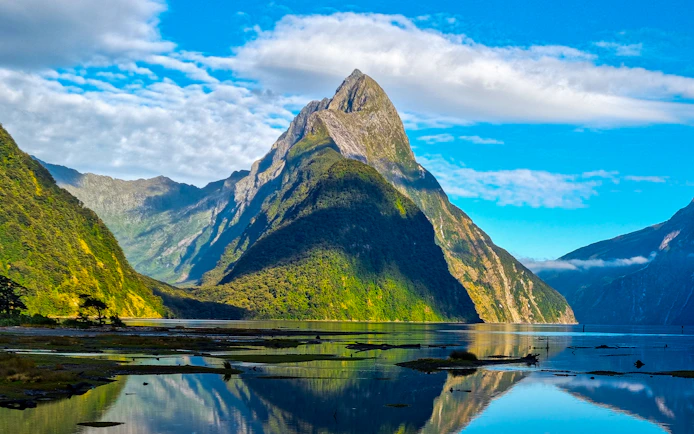Mitre Peak reflecting in Milford Sound, New Zealand, under a clear blue sky.