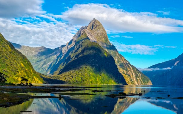 Mitre Peak reflecting in Milford Sound, New Zealand, under a clear blue sky.
