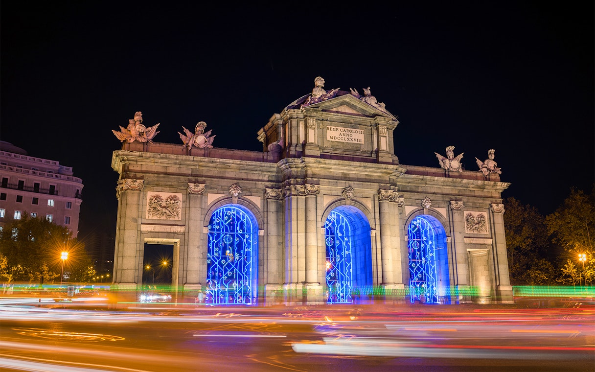 Puerta de Alcalá illuminated with blue Christmas lights in Madrid at night.