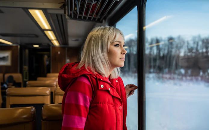 Woman gazing out train window at snowy landscape on Aurora Winter Train, Alaska.