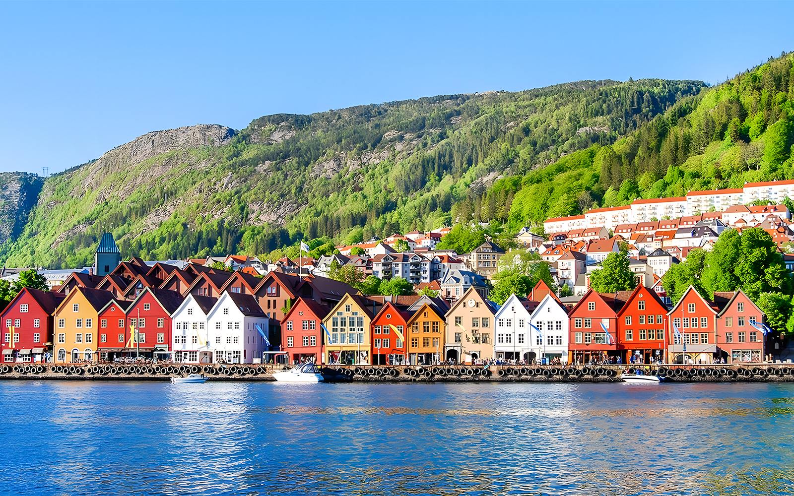 Colorful houses along the waterfront in Bergen, Norway, with green hills in the background.