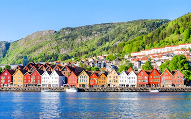 Colorful houses along the waterfront in Bergen, Norway, with green hills in the background.