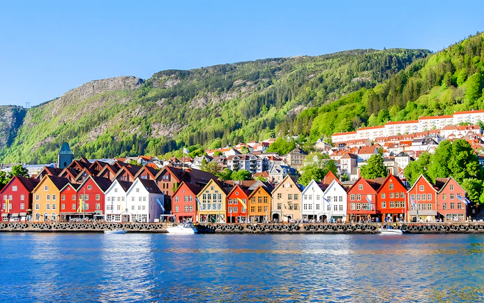 Colorful houses along the waterfront in Bergen, Norway, with green hills in the background.