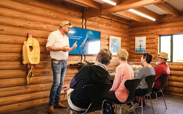 Crew conducting pre-flight briefing in a wooden cabin with a screen presentation.