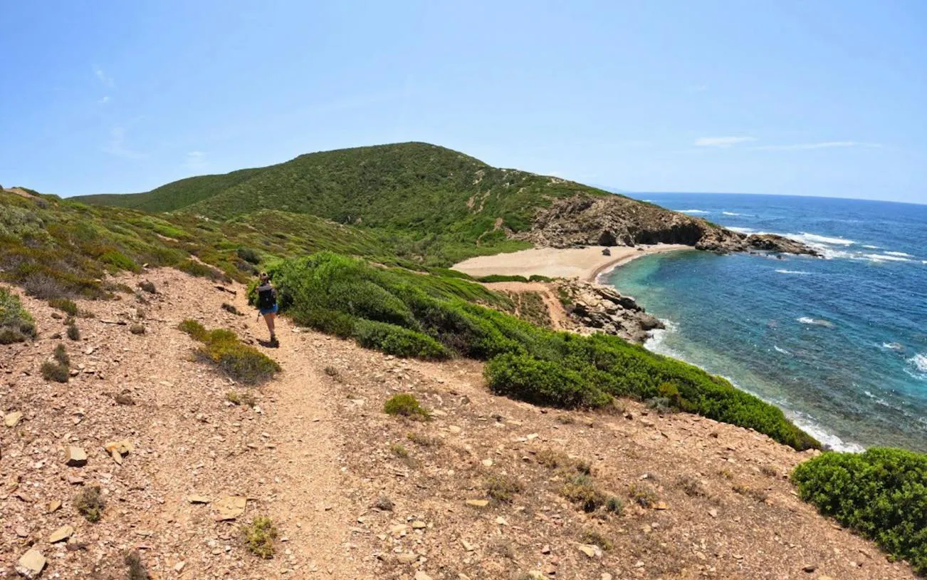 Trekker on coastal path overlooking cove and sea at Torre dei Corsari, Costa Verde, Oristano.