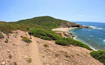 Trekker on coastal path overlooking cove and sea at Torre dei Corsari, Costa Verde, Oristano.