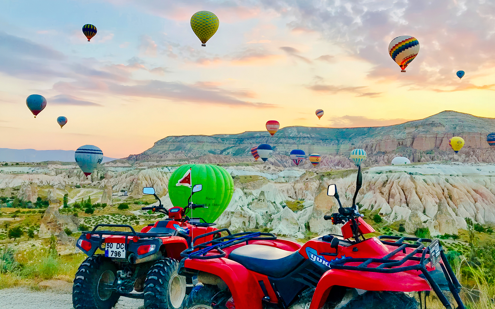ATVs parked with hot air balloons over Cappadocia landscape at sunset.