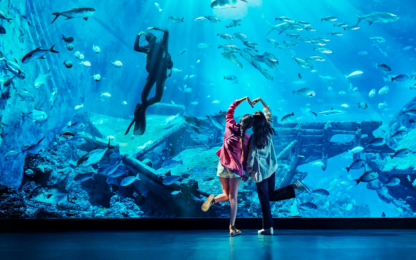 Women making heart shape in front of diver at S.E.A. Aquarium, Singapore.