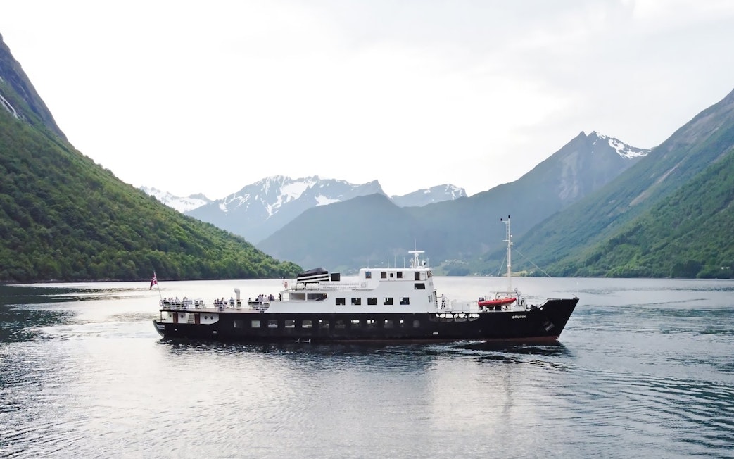 Sightseeing cruise ship on Hjørundfjord, surrounded by mountains, Norway.