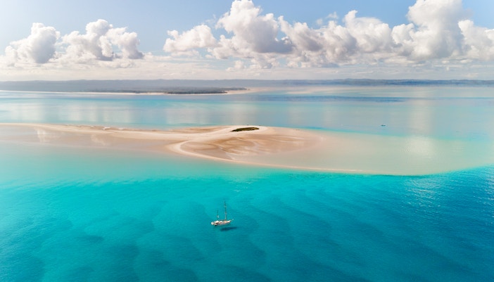 Sailboat near sandy Pelican Banks, Fraser Coast, with turquoise waters and distant shoreline.