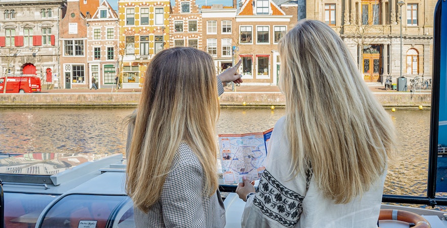 Two people on a canal cruise in Haarlem, Netherlands, pointing at historic buildings along the Spaarne River.