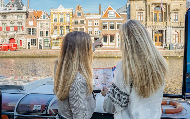 Two people on a canal cruise in Haarlem, Netherlands, pointing at historic buildings along the Spaarne River.