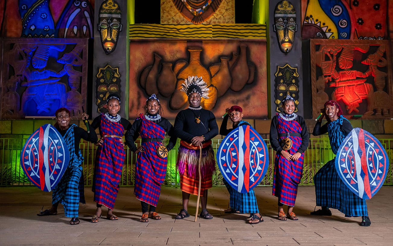 Performers in traditional attire with shields at Global Village attraction.