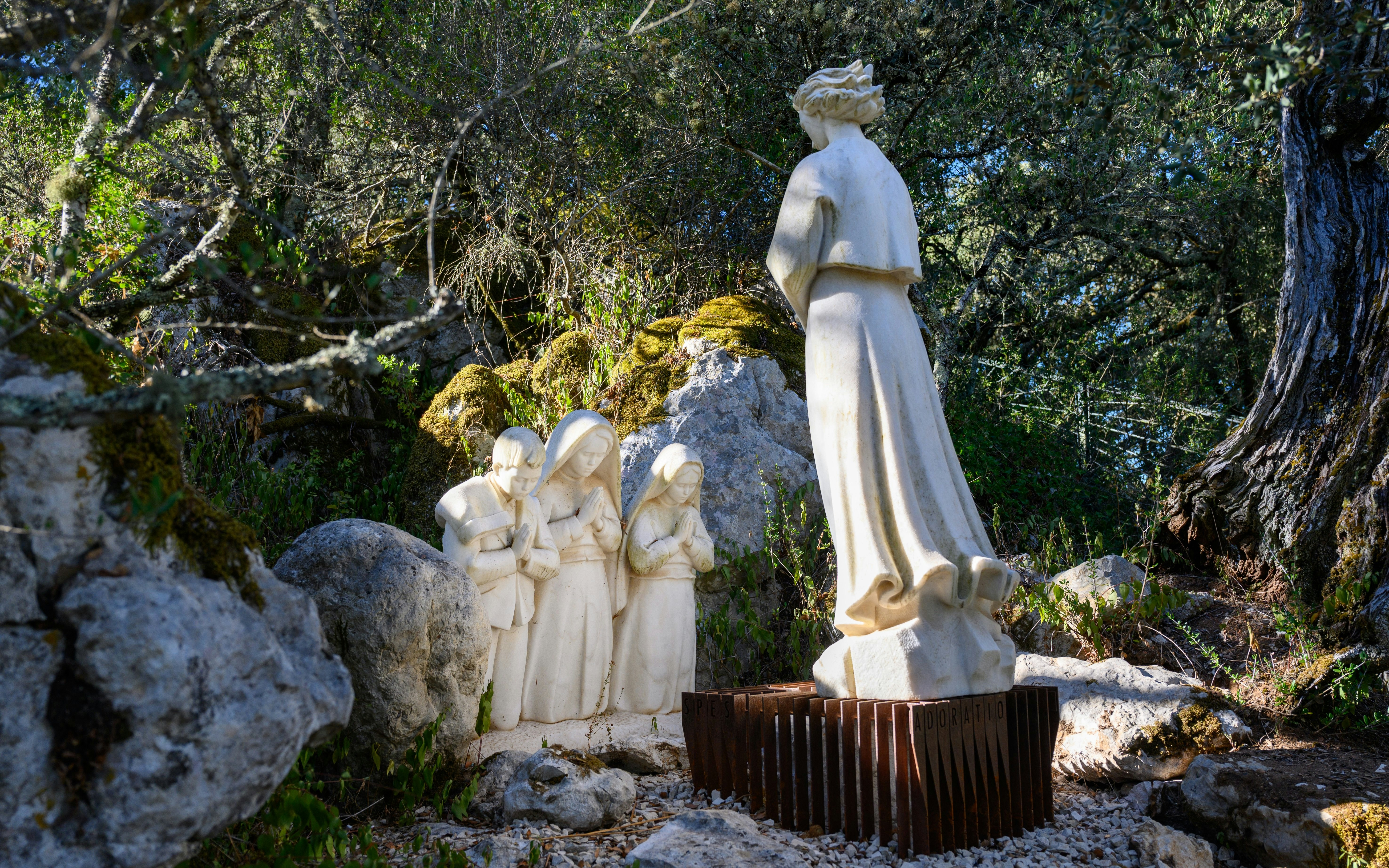 Statues of children and an angel in Valinhos, Fatima, surrounded by trees and rocks.