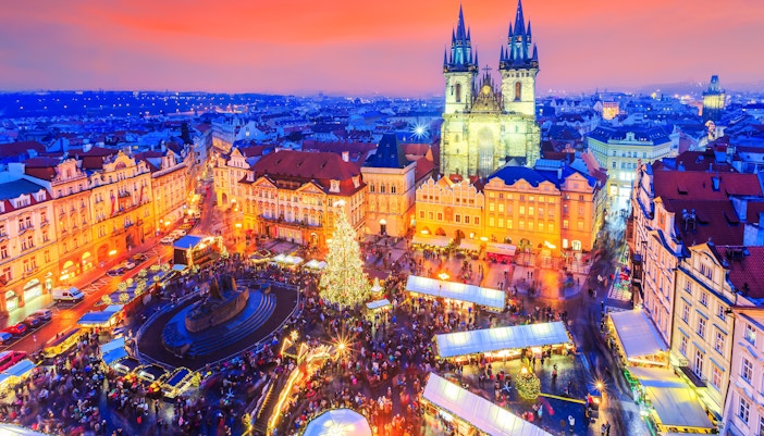 Old Town Square with Christmas market and lights in Prague, featuring Tyn Church at sunset.