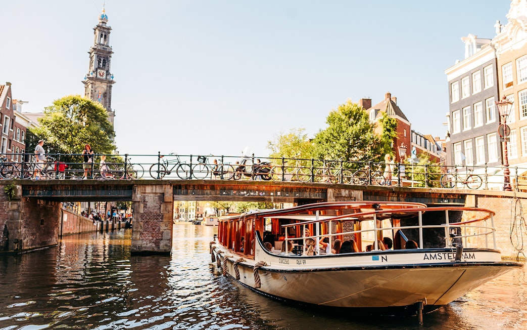 Amsterdam canal cruise boat passing under a bridge with Westerkerk tower in the background.